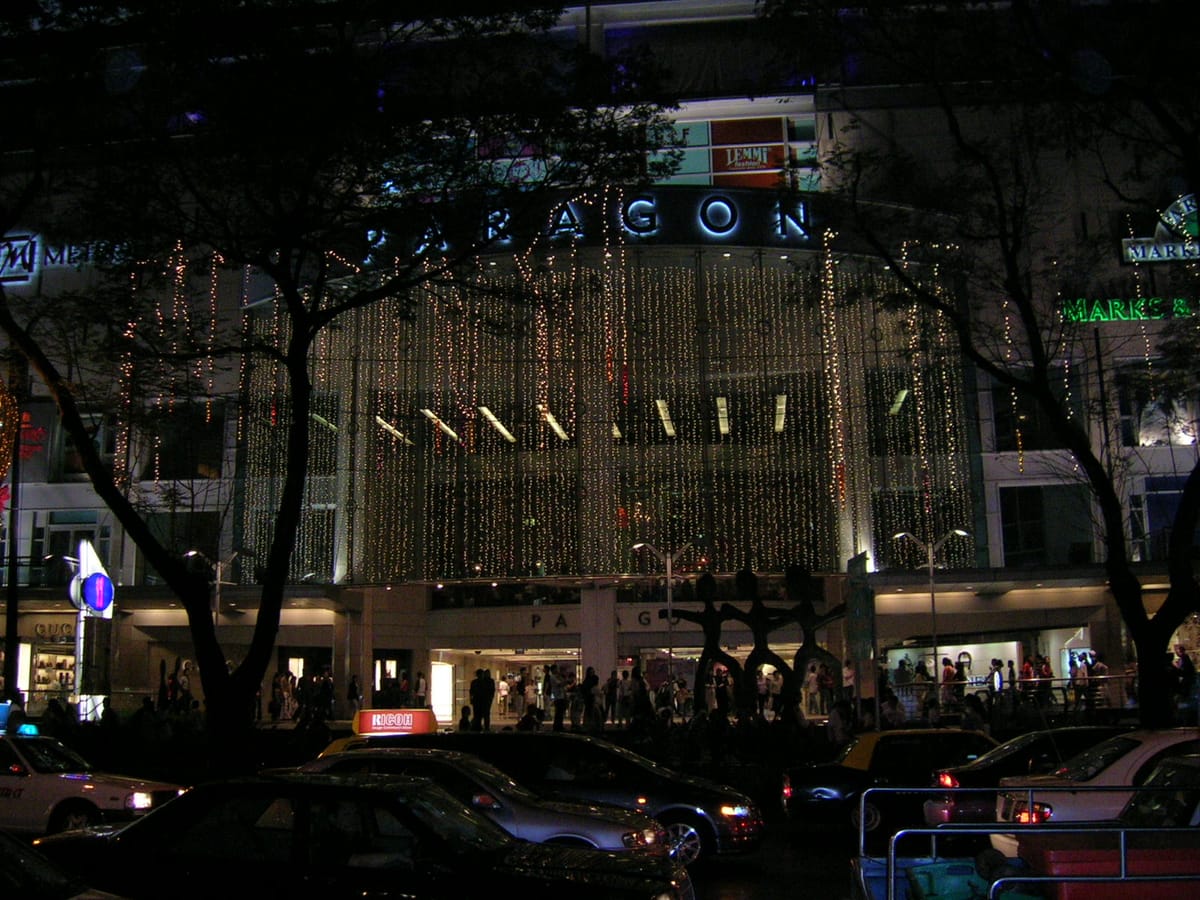 Night-time exterior of Paragon shopping mall on Orchard Road, illuminated with cascading lights, with Metro signage visible on the façade and shoppers near the entrance.