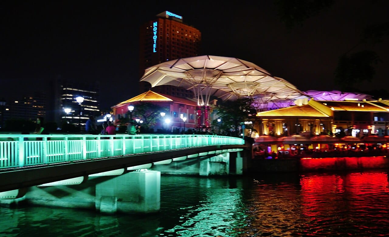 Clarke Quay and the Singapore River lit up at night with a pedestrian bridge and canopy-roofed riverside venues