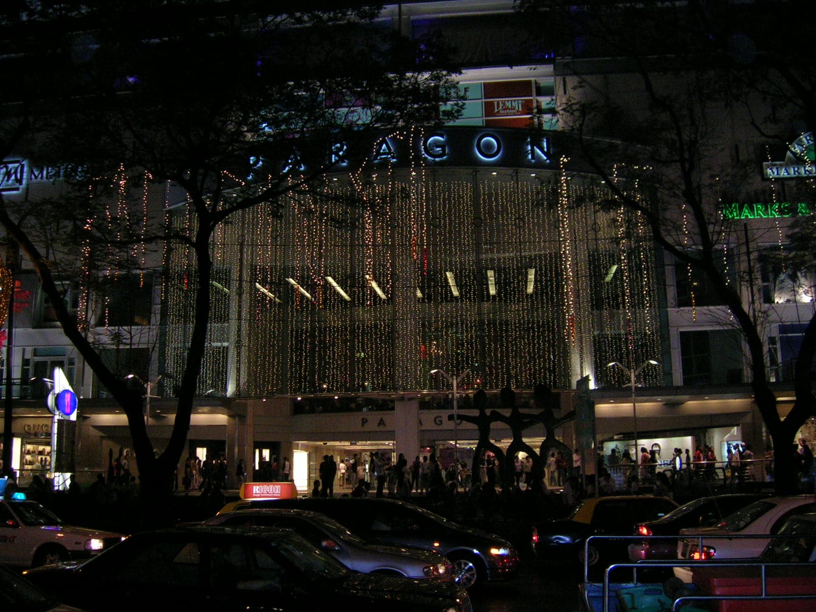 Night-time exterior of Paragon shopping mall on Orchard Road, illuminated with cascading lights, with Metro signage visible on the façade and shoppers near the entrance.