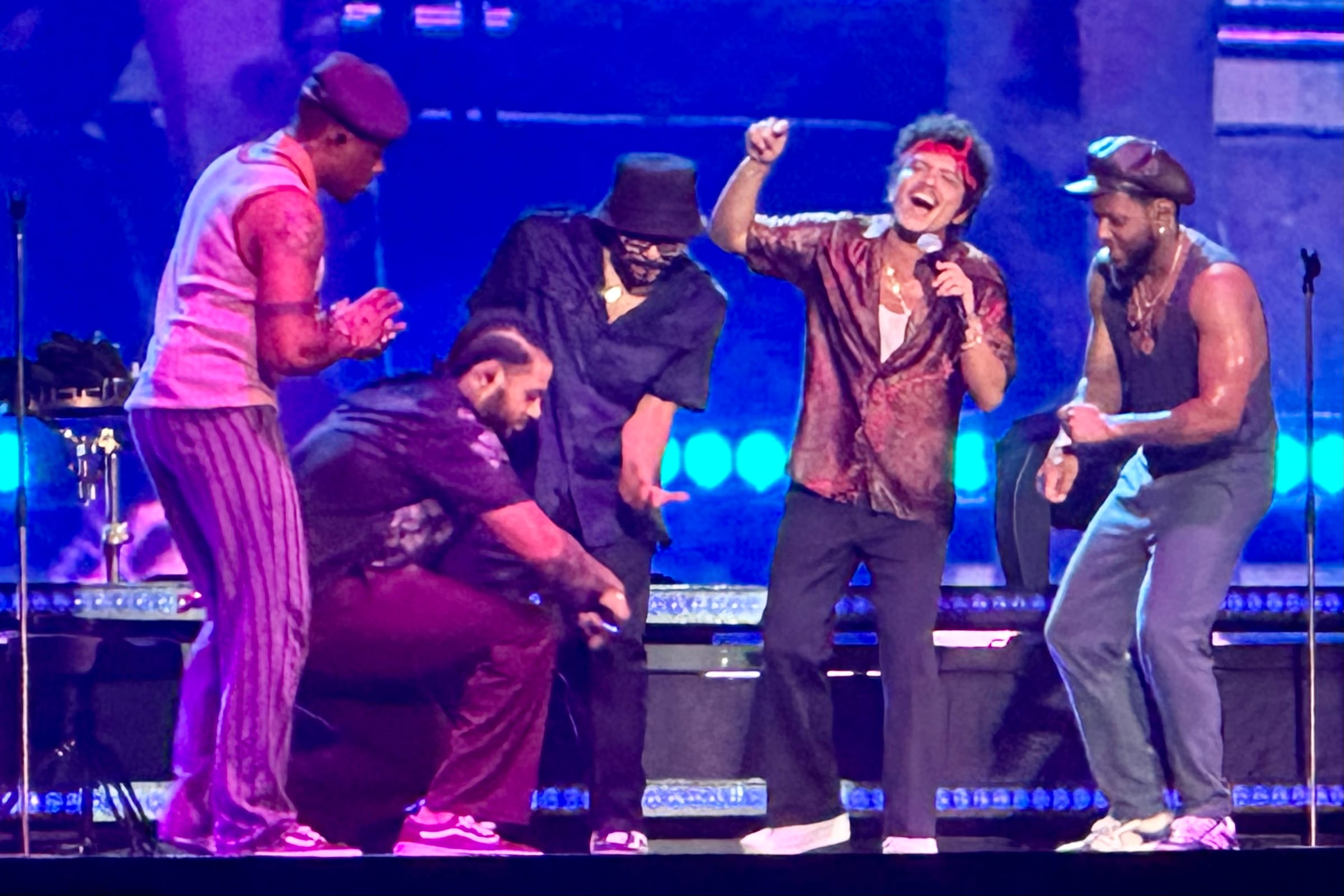 Bruno Mars laughs and sings in a red headband among four performers under blue stage lights at Singapore National Stadium in April 2024.