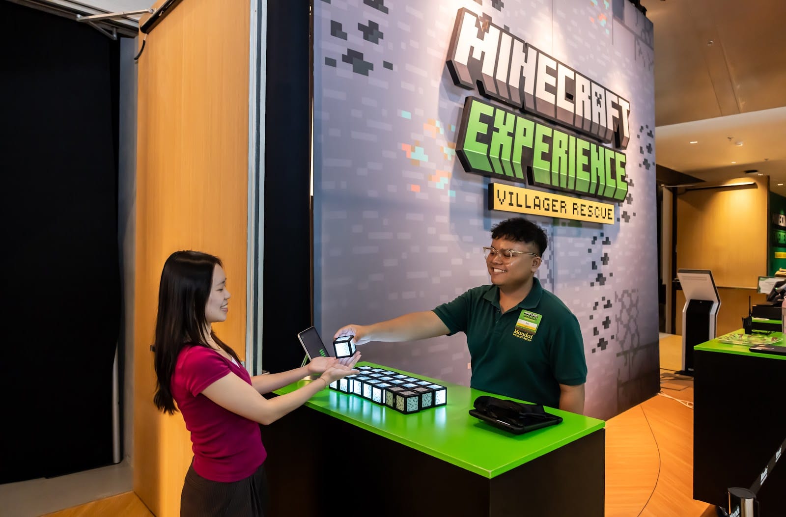 A visitor receives an Orb of Interaction from a staff member at the Minecraft Experience: Villager Rescue welcome area at Mandai.
